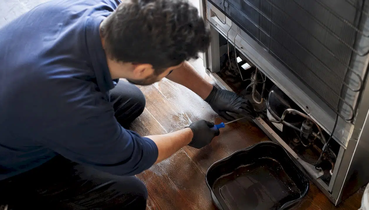 Hands clearing refrigerator defrost drain blockage